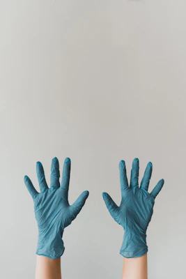Two hands wearing blue nitrile gloves raised against a plain light grey background