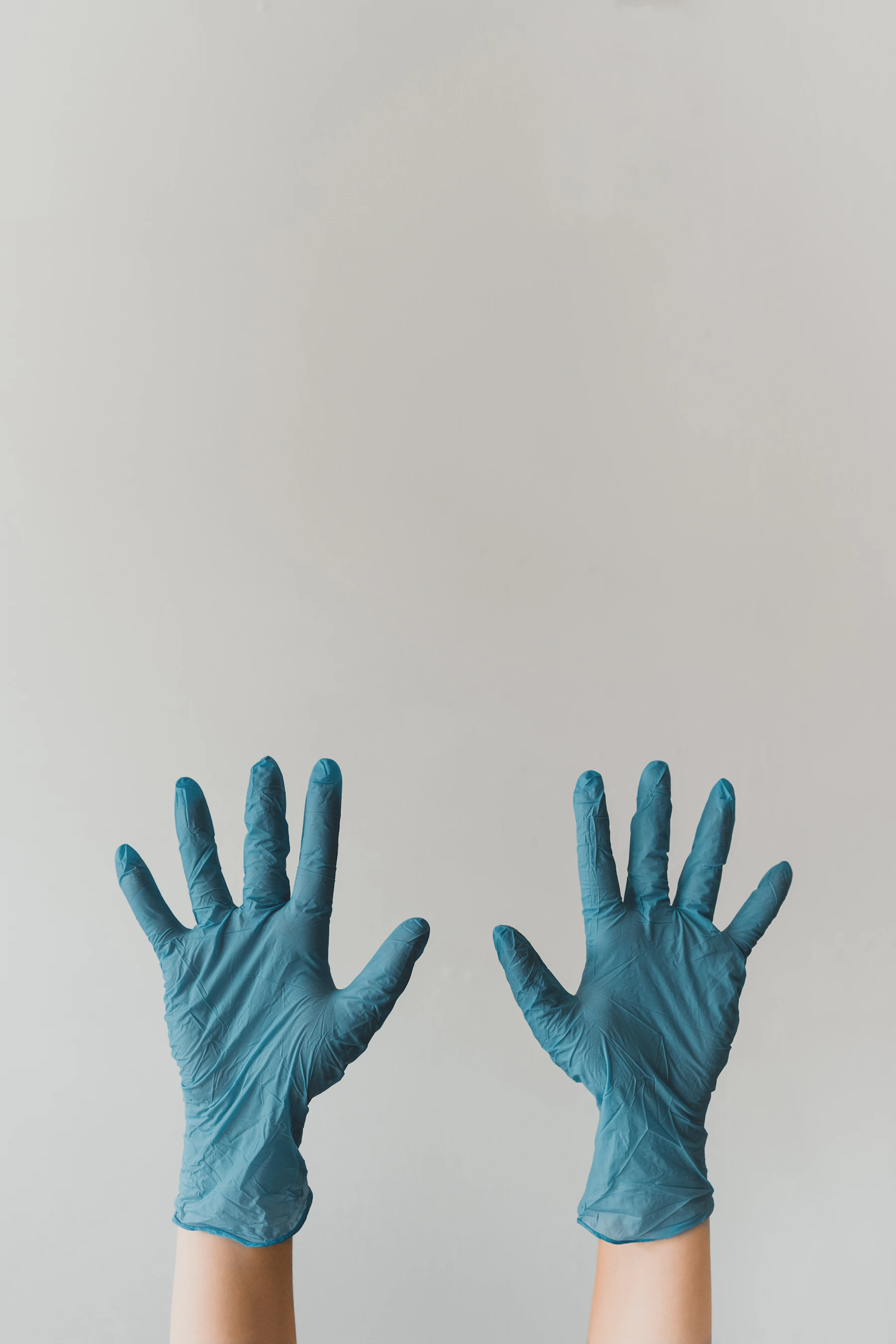 Two hands wearing blue nitrile gloves in a clinical setting