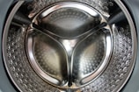 Close-up view of the interior of a stainless steel washing machine drum with a reflective surface and perforated pattern.