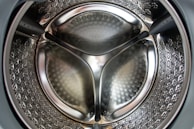 Close-up view of the interior of a stainless steel washing machine drum with a reflective surface and perforated pattern.