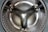 Close-up view of the interior of a stainless steel washing machine drum with a reflective surface and perforated pattern.