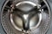 Close-up view of the interior of a stainless steel washing machine drum with a reflective surface and perforated pattern.