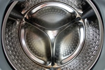 Close-up view of the interior of a stainless steel washing machine drum with a reflective surface and perforated pattern.