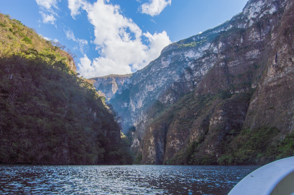 Montaña verde y gris al lado del cuerpo de agua bajo el cielo azul durante el día