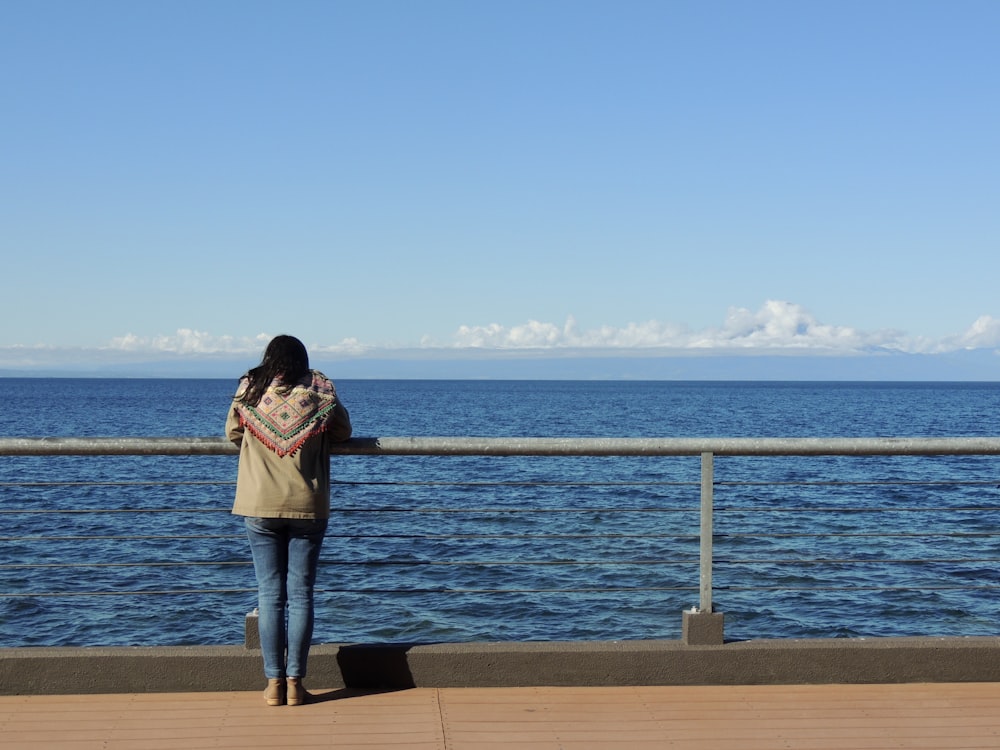 woman in pink jacket and blue denim jeans standing on dock during daytime