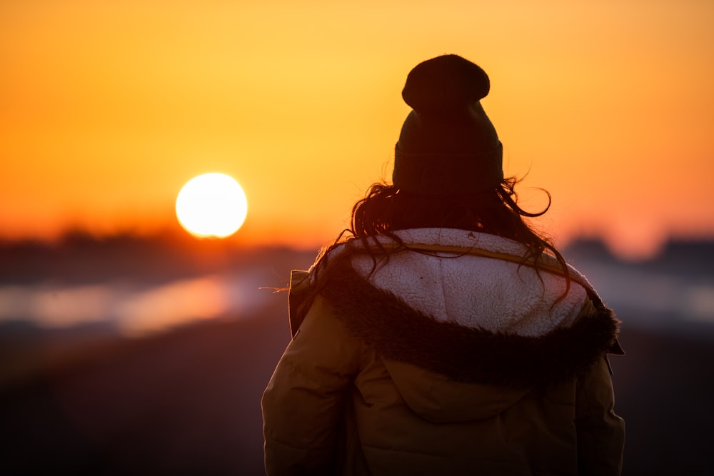 woman in brown jacket and black knit cap standing during sunset