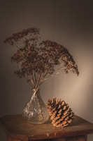Softly lit ceramic vase resting on a wooden table with dried wildflowers.