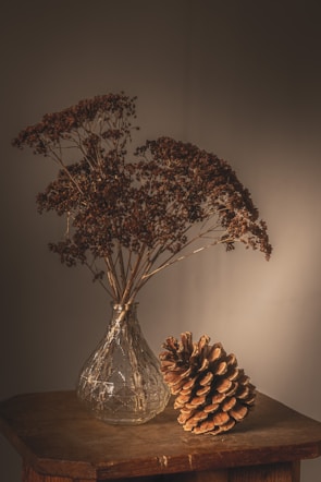 Softly lit ceramic vase resting on a wooden table with dried wildflowers.