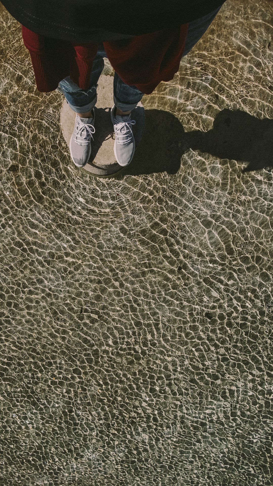 person in blue denim jeans and black shoes standing on brown sand