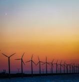 A wind farm at sunset with turbines turning gently against a colorful sky