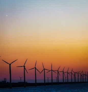 A wind farm at sunset with turbines turning gently against a colorful sky