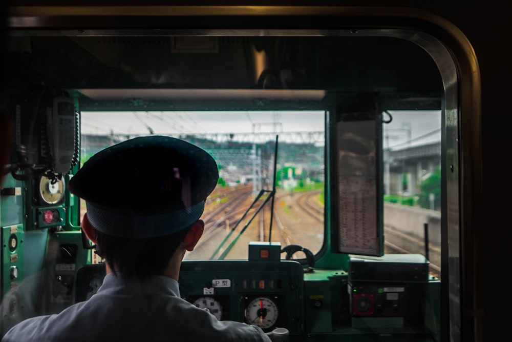 man in white shirt and black cap standing in front of green train during daytime