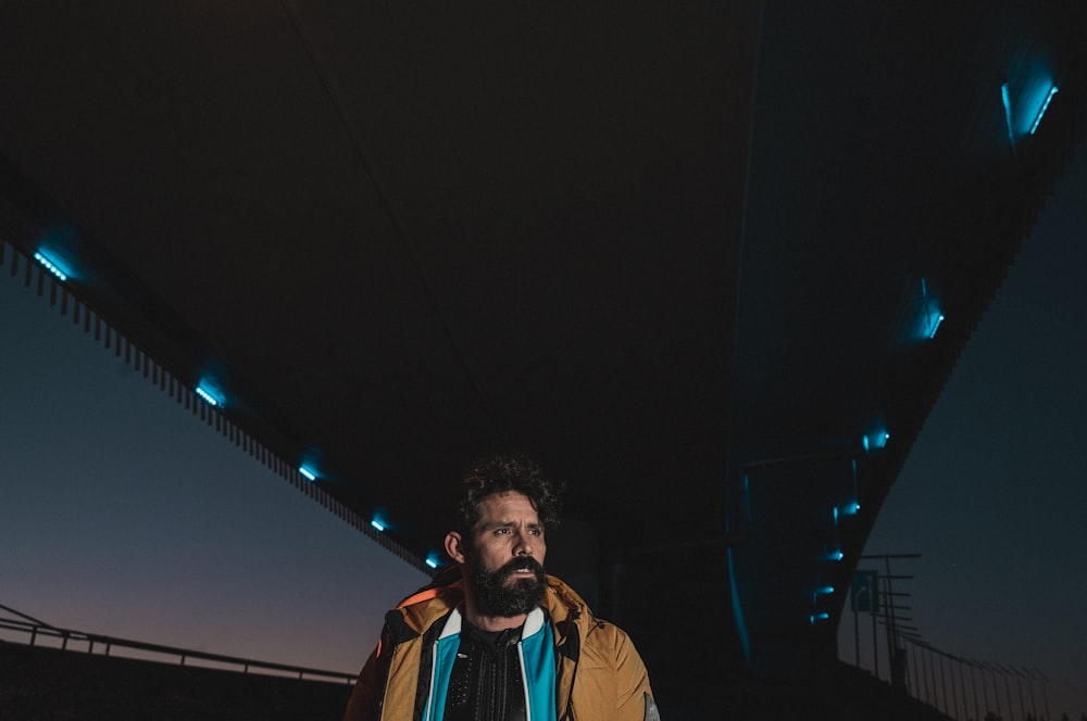 man in brown jacket standing near light post during night time