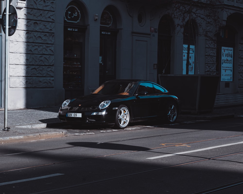 Porsche 911 negro estacionado cerca de un edificio de concreto blanco durante el día