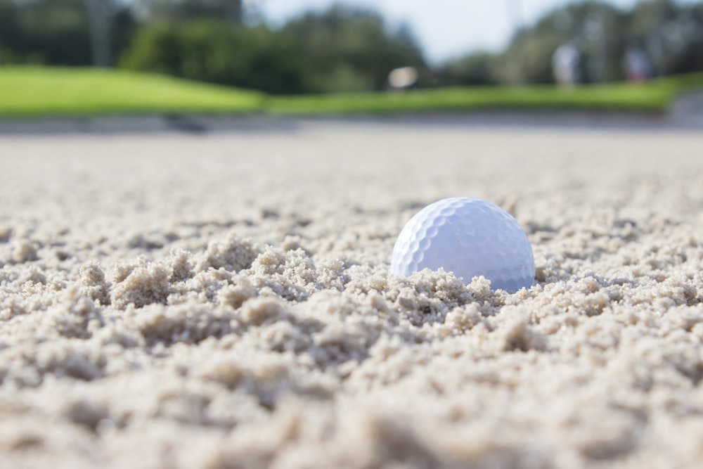 weißer Golfball tagsüber auf braunem Sand