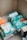 Several packages of Pampers baby diapers are arranged in an indoor setting. The packages are primarily turquoise and display images of smiling babies on the front. Various sizes of diaper packs are visible, indicating different quantities and designs.