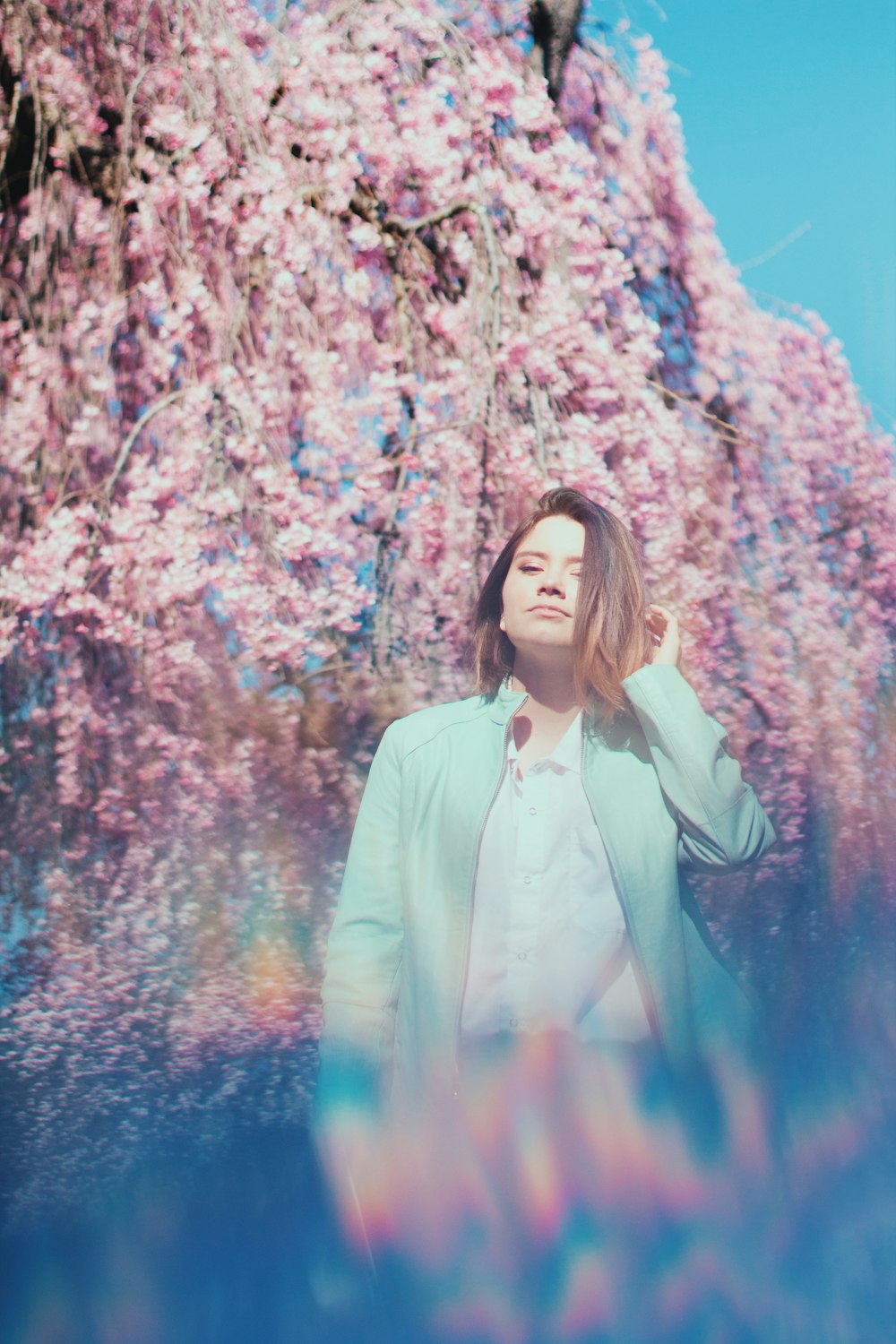 woman in white button up long sleeve shirt standing near pink leaf trees during daytime