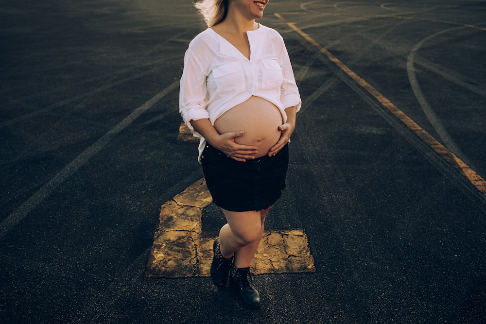 woman in white dress shirt and black skirt standing on gray asphalt road during daytime