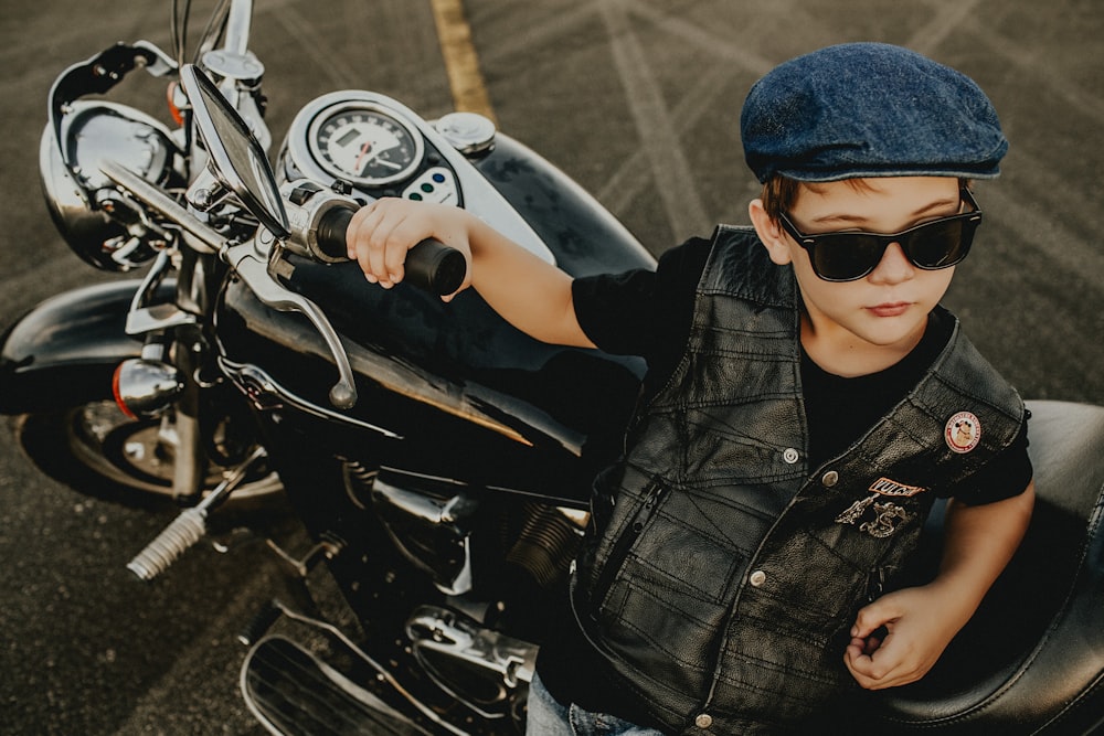 man in black leather jacket wearing blue cap riding on black motorcycle