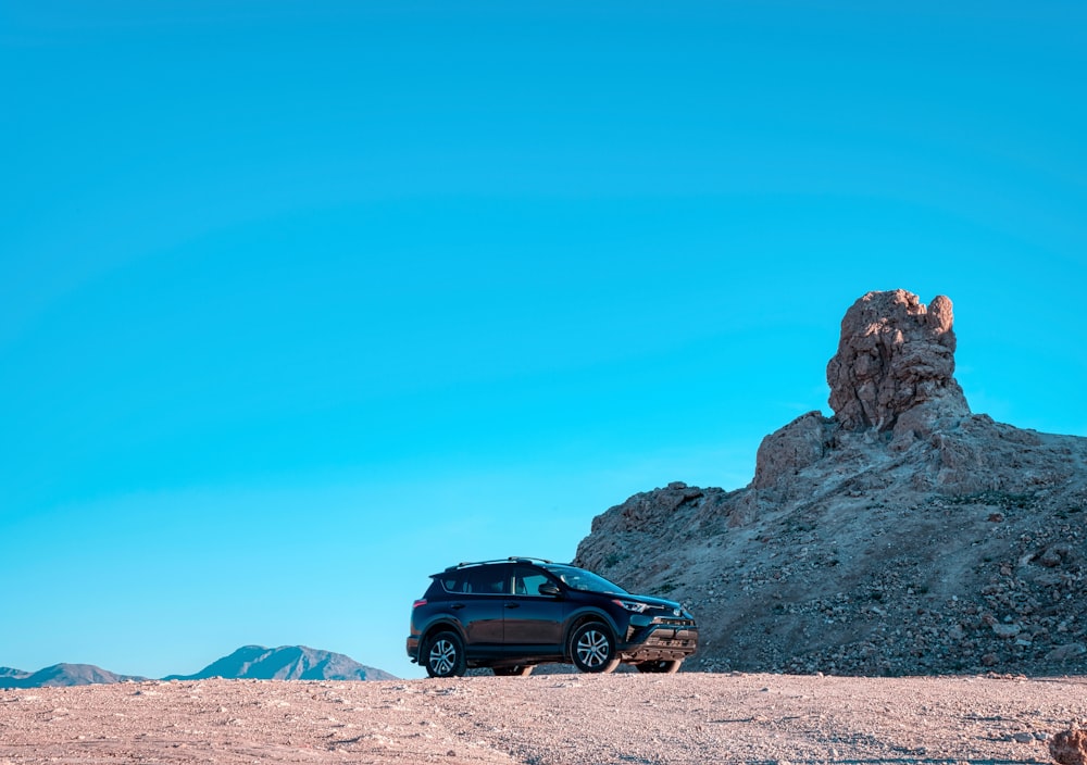 昼間の青空の下、茶色の砂浜に黒いSUV