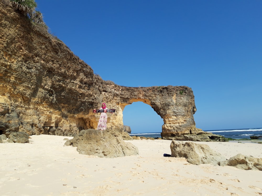 woman in pink dress standing on brown rock formation during daytime