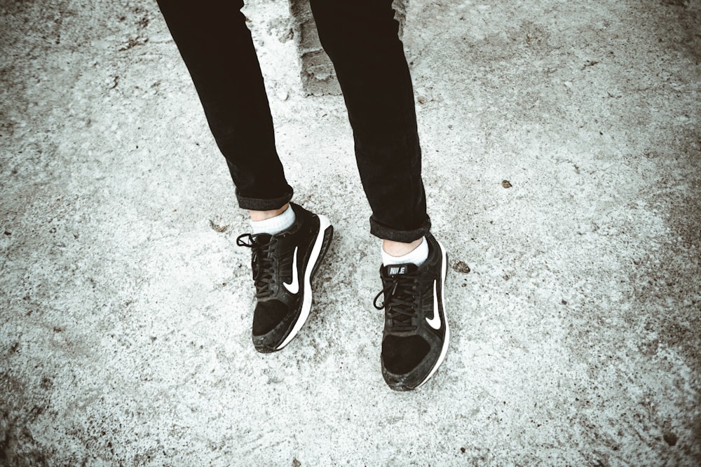 Person in schwarzen Hosen und schwarz-weißen Nike-Sneakers