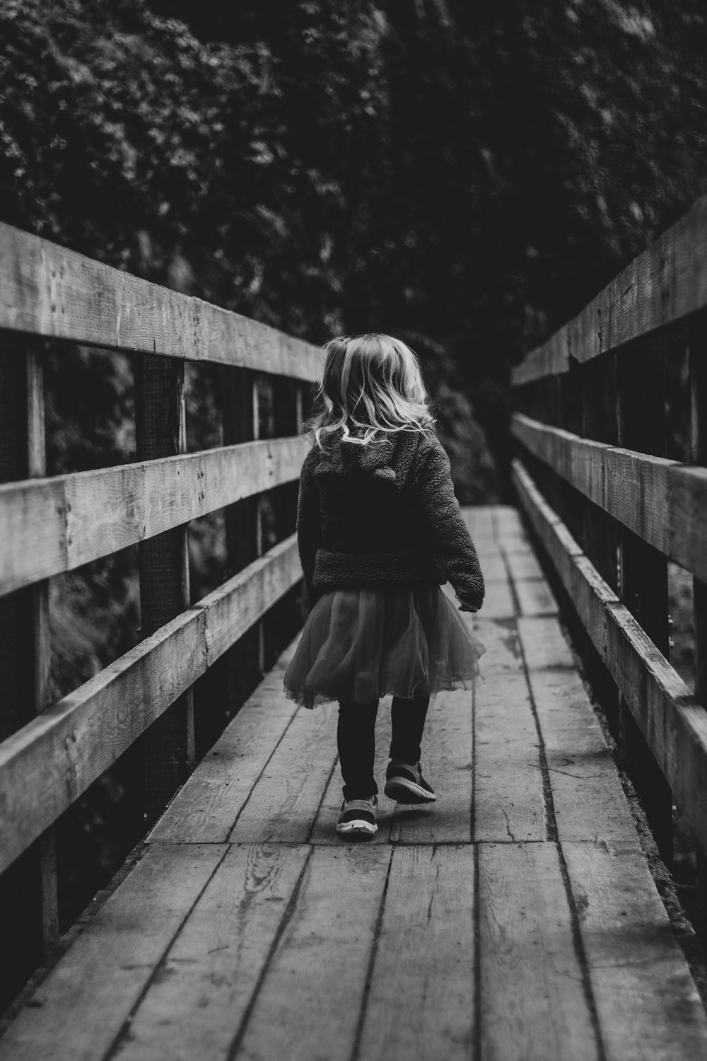 foto em escala de cinza da mulher que caminha na ponte de madeira