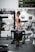 A woman is standing in a gym holding a heavy barbell plate marked with 'YORK 45'. She is wearing a cap, sports bra, and patterned leggings. The gym is equipped with various fitness machines and weights.