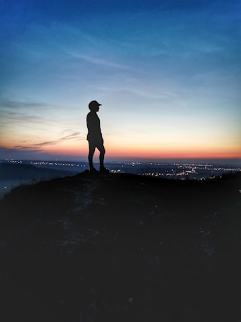 silhouette of man standing on seashore during sunset