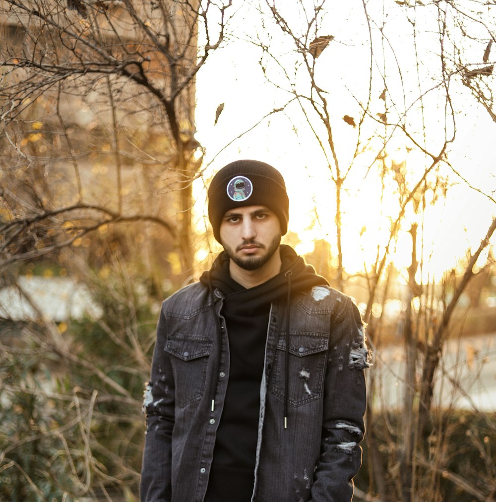 man in black leather jacket standing near bare trees during daytime