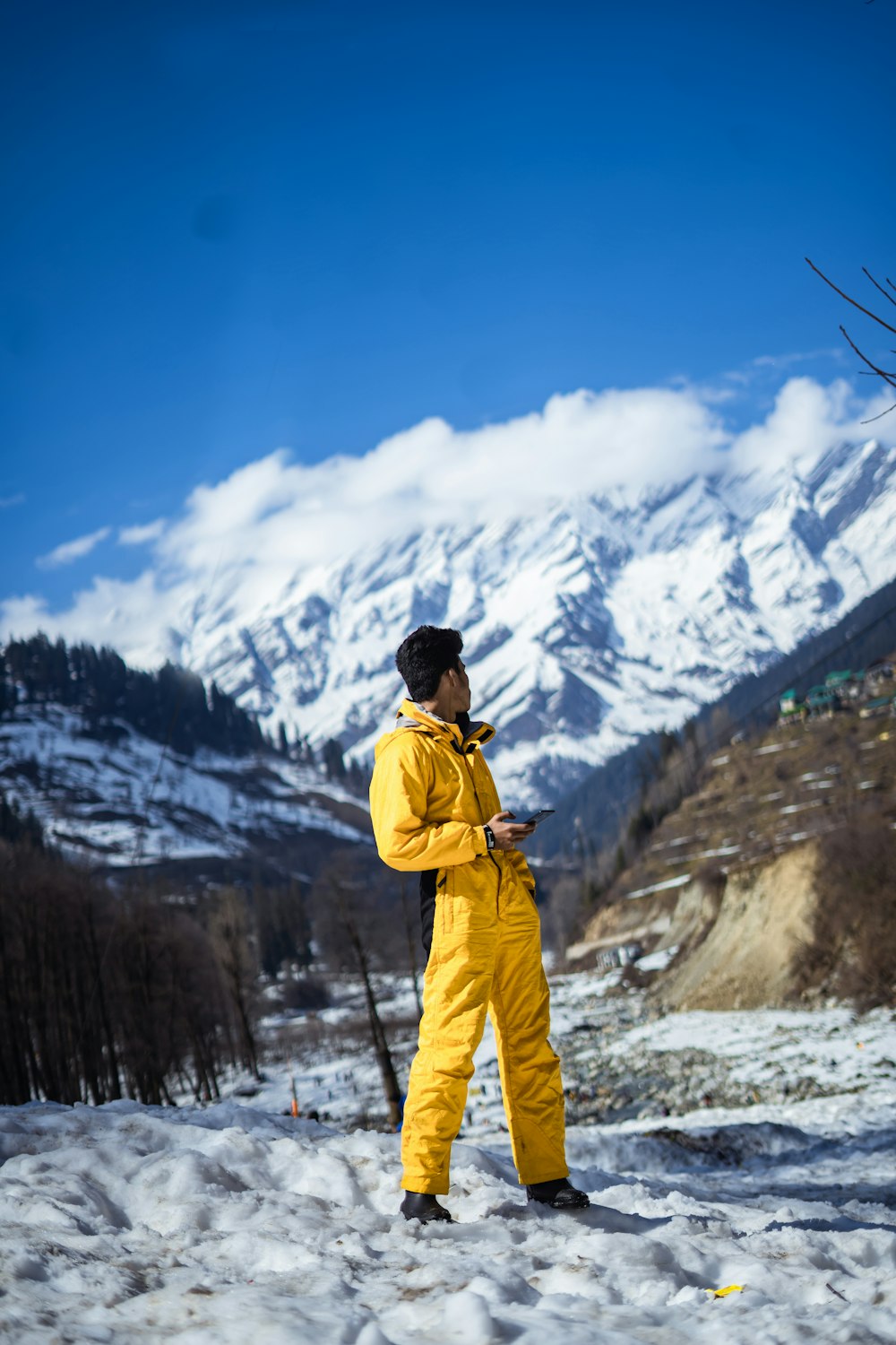 Mann in gelber Jacke und blauer Hose, der tagsüber auf schneebedecktem Boden steht