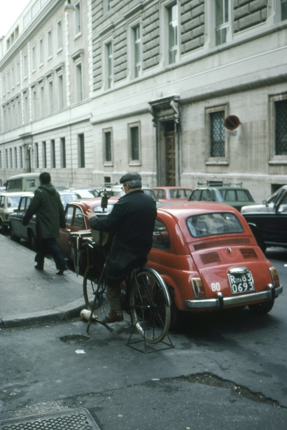 man in black jacket riding bicycle near red car during daytime