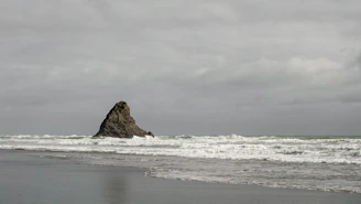 A solitary rock formation standing against crashing waves under a brooding sky.