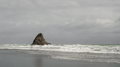 A solitary rock formation standing against crashing waves under a brooding sky.