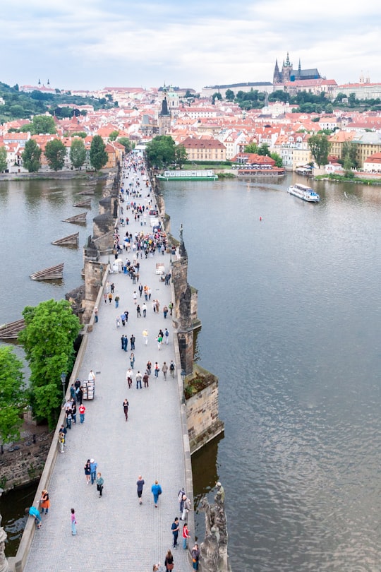 people walking on gray concrete bridge over river during daytime in Praha Czech Republic