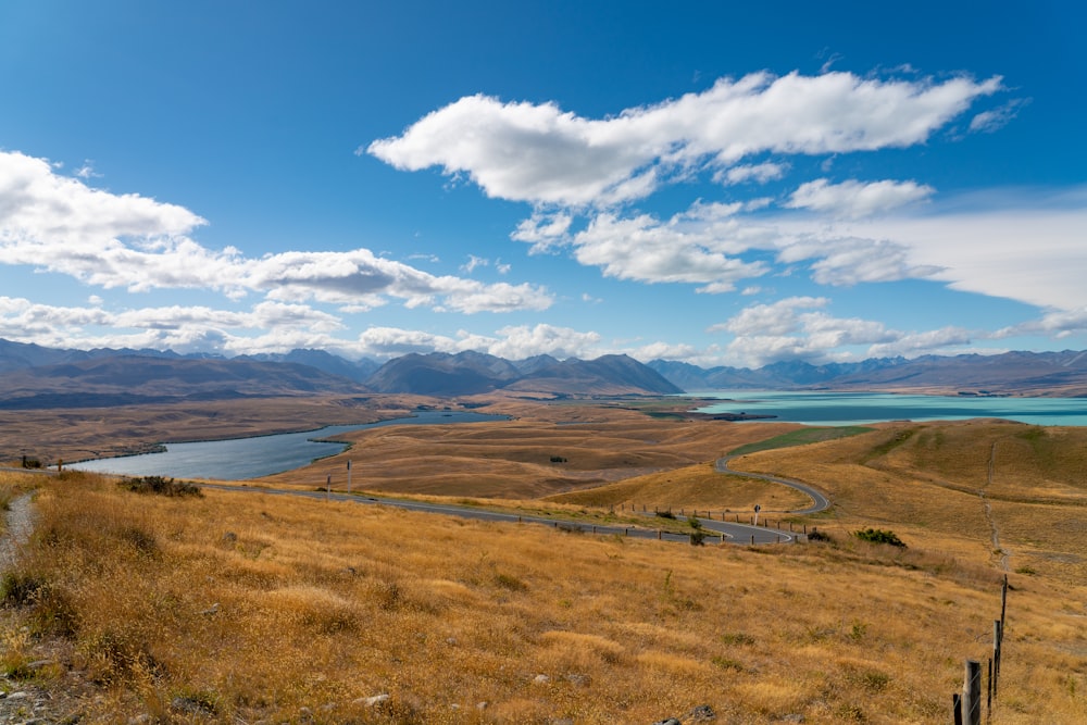 brown grass field near body of water under blue sky during daytime