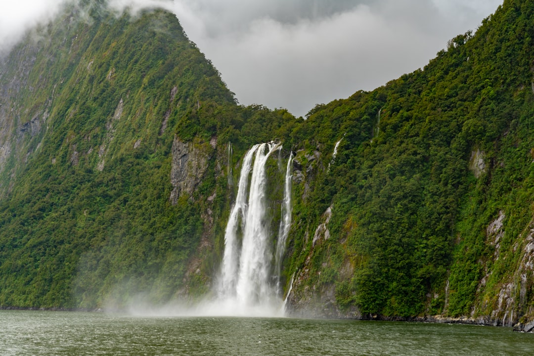 waterfalls near green trees under white clouds during daytime