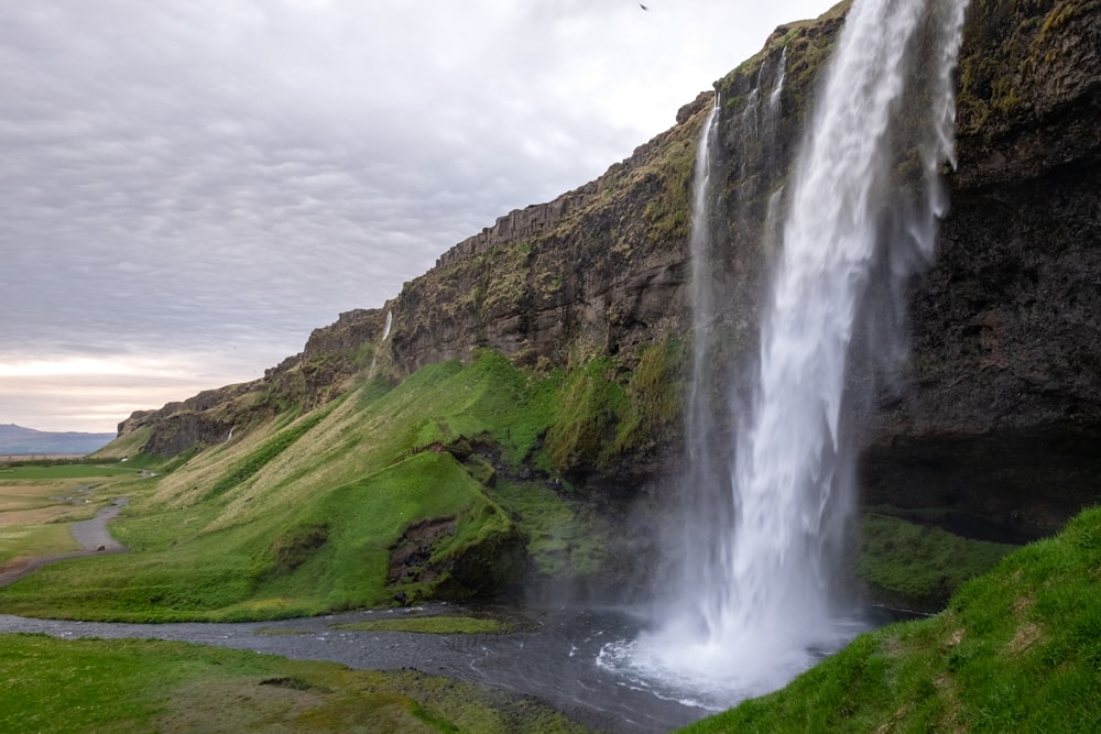 waterfalls on green grass covered hill under white cloudy sky during daytime