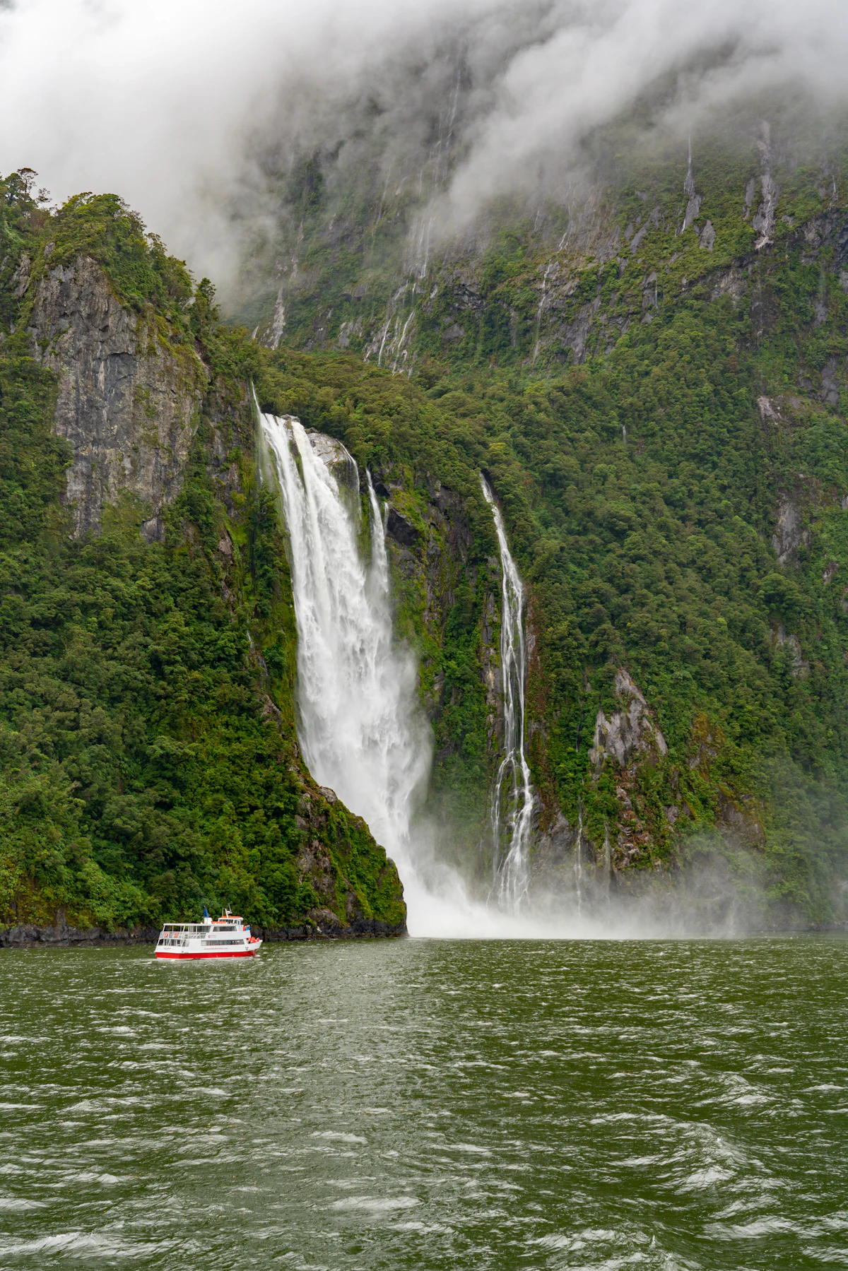 A cruise boat beneath a waterfall in Milford Sound