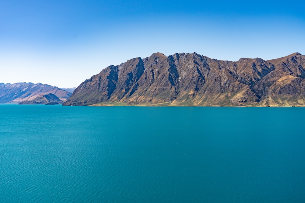 brown rocky mountain beside blue sea under blue sky during daytime