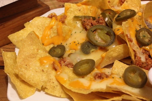 A close-up view of nachos topped with melted cheese, jalapeño slices, and ground meat, all served on a white plate.