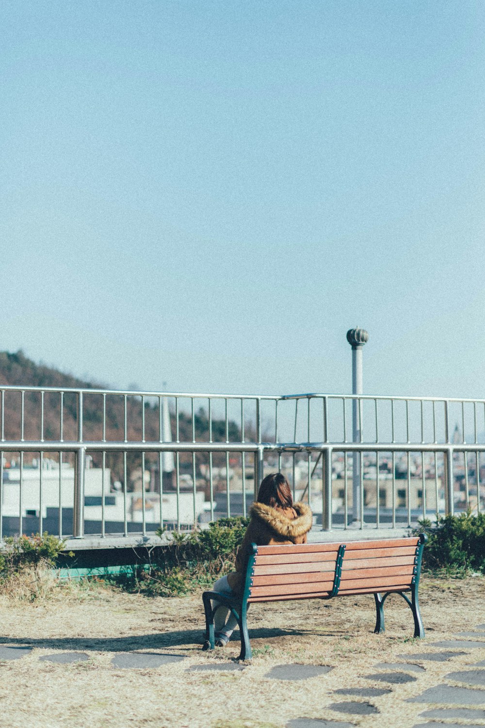 Femme en veste noire assise sur un banc en bois brun pendant la journée