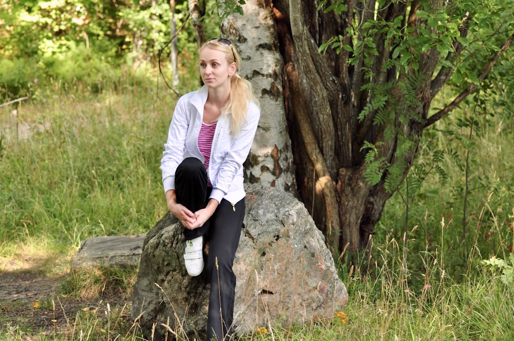 woman in white long sleeve shirt and black pants sitting on gray rock