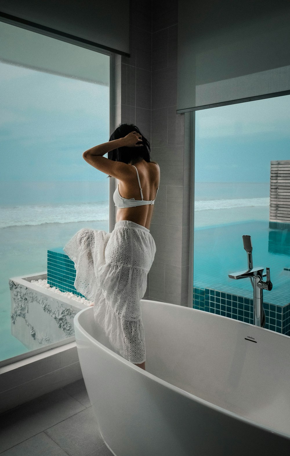 woman in white brassiere and blue denim jeans sitting on white ceramic bathtub