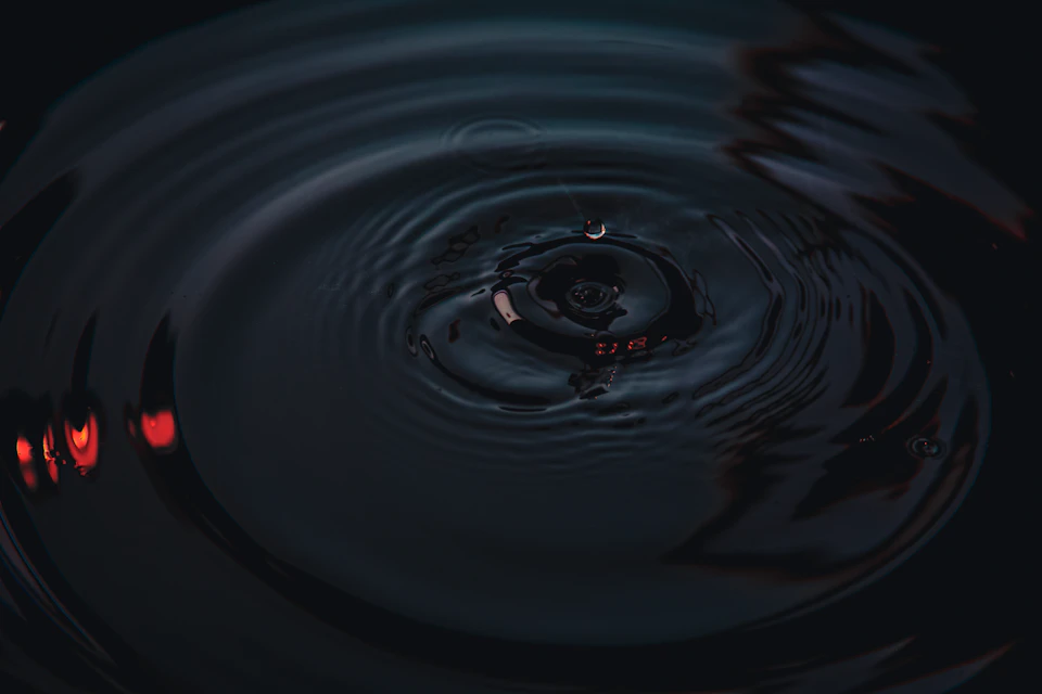 Close-up view of a small drop of water creating a circular pattern on dark water