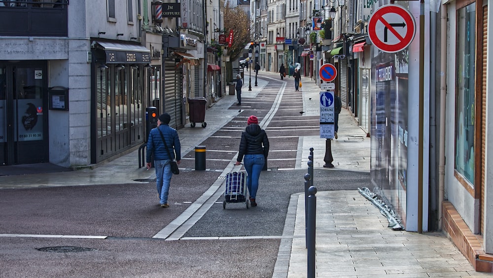 Hombre con chaqueta azul y jeans de mezclilla azul caminando en la acera durante el día