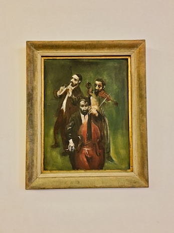 A framed painting depicting three musicians playing instruments; one is playing a flute, another a violin, and the third a cello. The background is a dark, earthy green that enhances the musicians' focused expressions and postures.