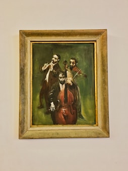 A framed painting depicting three musicians playing instruments; one is playing a flute, another a violin, and the third a cello. The background is a dark, earthy green that enhances the musicians' focused expressions and postures.