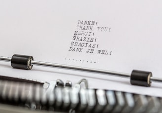 A close-up of a typewriter with a sheet of paper in it. The paper contains the word 'thank you' typed in multiple languages, including German, English, French, Italian, Spanish, and Dutch.