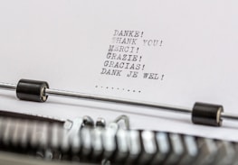 A close-up of a typewriter with a sheet of paper in it. The paper contains the word 'thank you' typed in multiple languages, including German, English, French, Italian, Spanish, and Dutch.